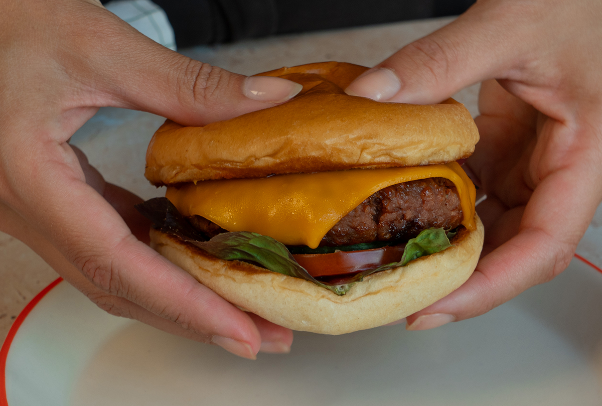 2 Hände halten einen Cheeseburger mit Gurken Kimchi