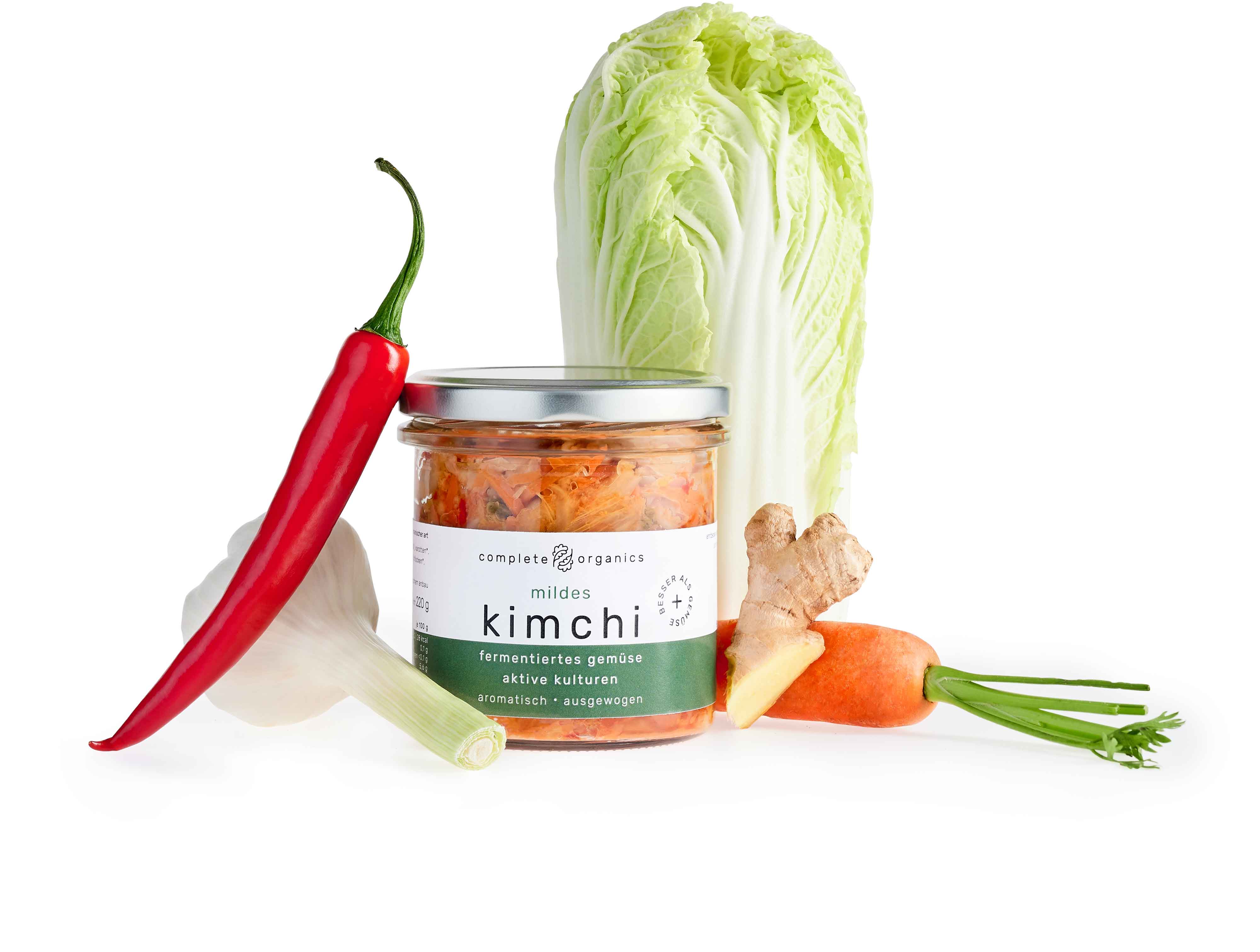 Fermentiertes Mildes Kimchi im Glas mit Chinakohl, Karotte, Ingwer, Knoblauch und Chilischote im Hintergrund