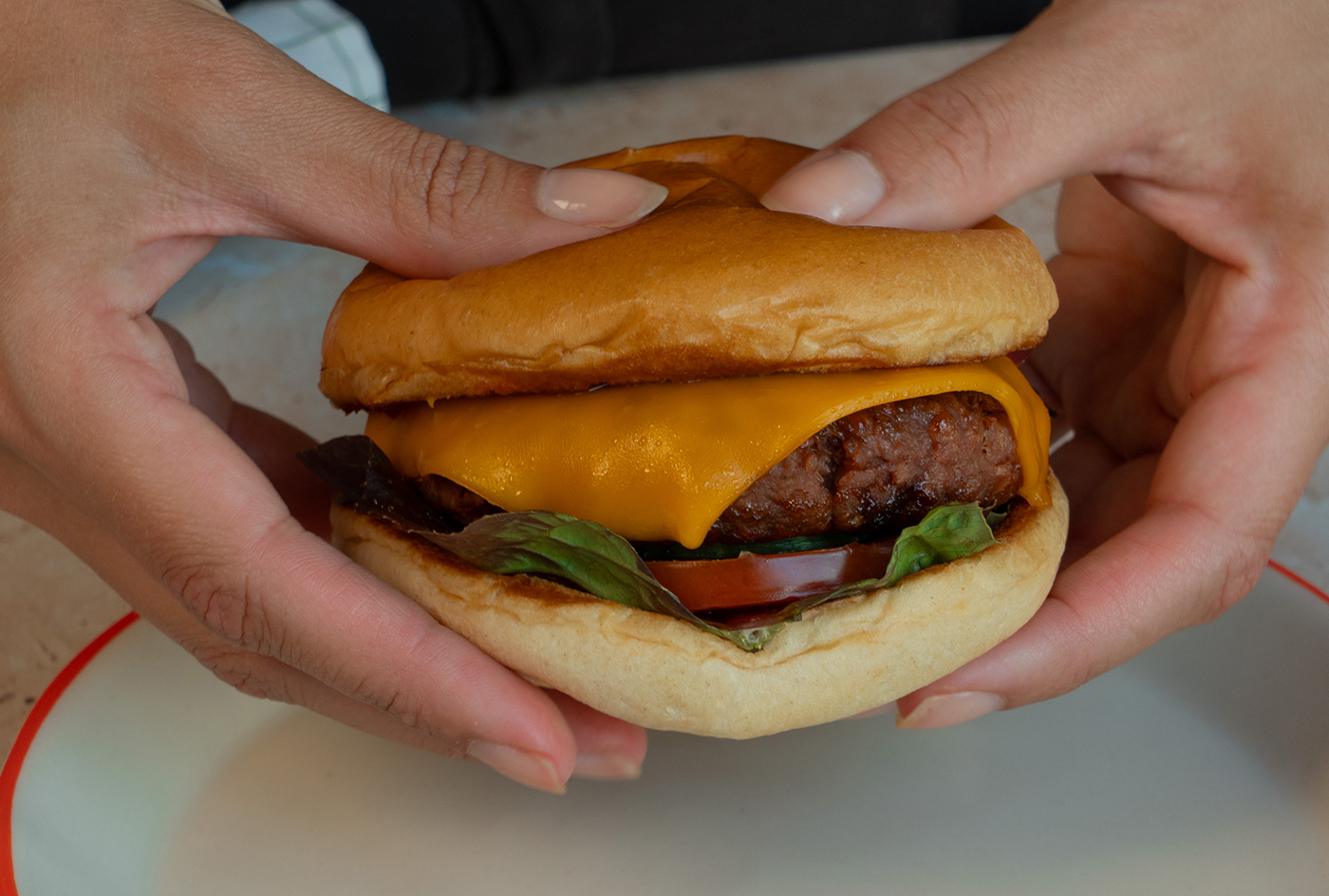 2 Hände halten einen Cheeseburger mit Gurken Kimchi